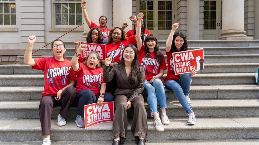 LanguageLine Solutions workers sit on steps of NYC City Hall with their fists in the air. 